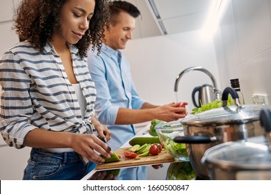 Young multiethnic couple having romantic date at home standing at kitchen cooking dinner together husband washing vegetables while wife cutting ingredients smiling concentrated close-up - Powered by Shutterstock