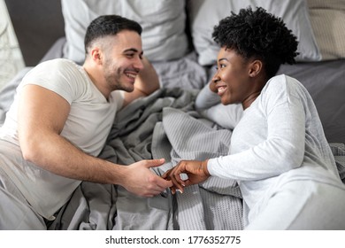 Young multiethnic couple holding hands while lying in bed in morning