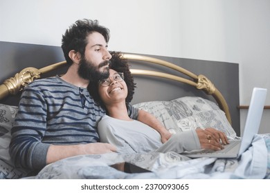 young multiethnic couple indoor using computer sitting bed 