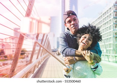 Young multiethnic couple outdoor in the city back light, taking selfie with smart phone and selfie stick, hugging - vanity, social network, technology concept - Powered by Shutterstock