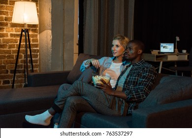 Young Multiethnic Couple With Popcorn Watching Film Together On Sofa At Home