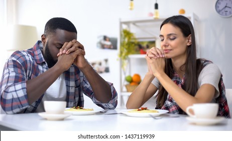 Young multiethnic couple praying before lunch, thanking God for meal, religion - Powered by Shutterstock