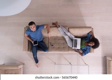 Young Multiethnic Couple Relaxes In The Luxury Living Room, Using A Tablet And Laptop Computer Top View