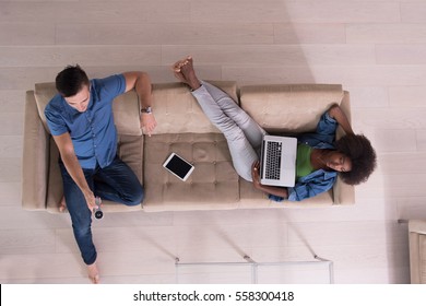 Young Multiethnic Couple Relaxes On The Sofa In The Luxury Living Room, Using A Tablet And Remote Control Top View