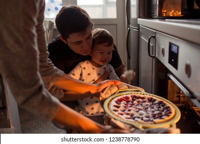 Young Multiethnic Family Making A Cake Together. Mom Dad And Son Pull The Cake Out Of The Oven