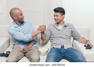 young multiethnic friends handshaking while sitting and playing video games at home - Shutterstock ID 659749216