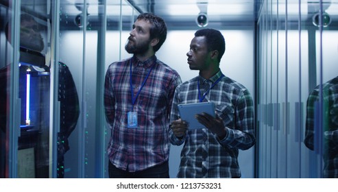 Young multiethnic men using tablet and diagnosing server hardware while walking in data center corridor