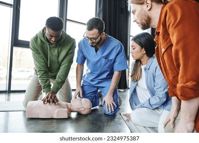 young multiethnic people and medical instructor looking at african american man doing chest compressions on CPR manikin, cardiopulmonary resuscitation, first aid training seminar - Powered by Shutterstock