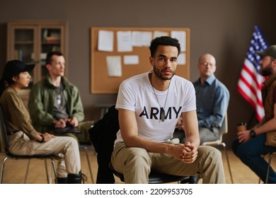 Young Multi-ethnic Unhappy Man In Casualwear Sitting Against Counselor And Several Intercultural Attendants Of PTSD Support Group