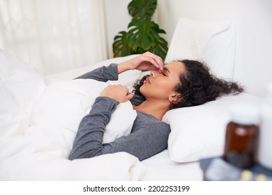 A young multi-ethnic woman holds her nose in pain lying in bed with migraine - Shutterstock ID 2202253199