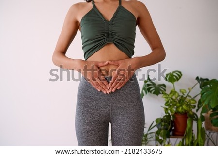 A young multi-ethnic woman holds her hands to her stomach, illustrate gut health