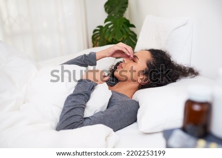 A young multi-ethnic woman holds her nose in pain lying in bed with migraine
