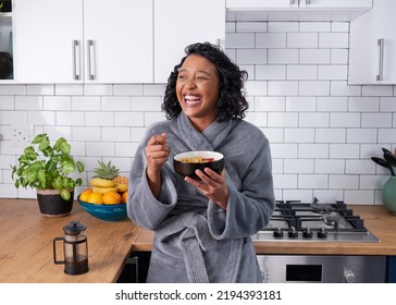 A Young Multi-ethnic Woman Laughs While Eating Breakfast Cereal In Dressing Gown