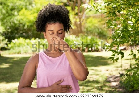 A young multi-ethnic woman practices alternate nostril breathing, yoga in garden