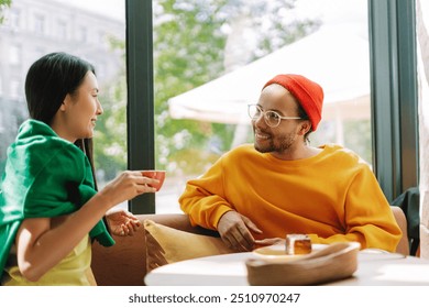 Young multiracial Asian woman and Latin man are happily chatting in a cafe, enjoying coffee and each other's company. The cafe has a bright and airy atmosphere. Friendship concept - Powered by Shutterstock