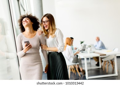 Young multiracial businesswomen smiling, while other businesspeople working in background at the office - Shutterstock ID 1010313442