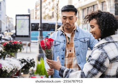 Young multiracial couple is choosing red roses at a flower market stall, celebrating valentine's day with a romantic gesture of love and appreciation - Powered by Shutterstock