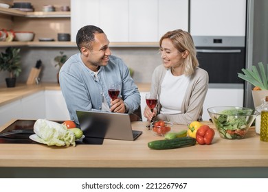 Young Multiracial Couple Communicating With Kids Or Relatives, Having Video Chat On Laptop Computer From Home At Modern Kitchen While Drinking Red Wine.