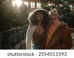 Young multiracial couple enjoying a romantic date at the botanical garden, embracing and looking up with smiles, surrounded by lush greenery