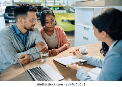 Young multiracial couple going through paperwork with saleswoman during a meeting in showroom.  - Powered by Shutterstock