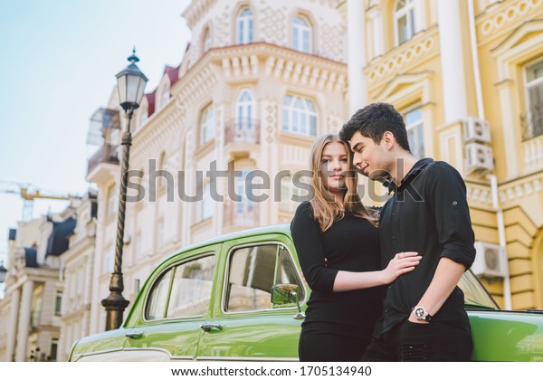 Young multiracial couple,\
male and female lovers heterosexual people students. Beautiful\
models posing standing near a retro car in the city. Dressed in\
black clothes.
