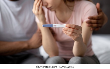 Young Multiracial Couple With Positive Pregnancy Test Feeling Upset, Facing Unplanned Childbearing, Having Problems, Selective Focus. Millennial Woman Crying, Her Husband Supporting Her At Home