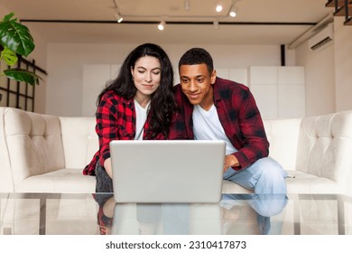 young multiracial couple sitting on comfortable sofa and looking into laptop at home, african american man with european woman using computer, interracial family looking into laptop - Powered by Shutterstock