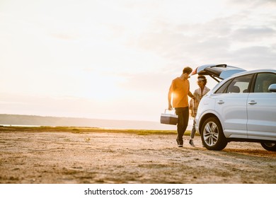 Young multiracial couple standing with cooler bag on field during car trip