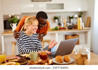 Young multiracial couple talking and using a laptop over breakfast at home - Powered by Shutterstock - Get 15% off with code: PIKWIZARD15
