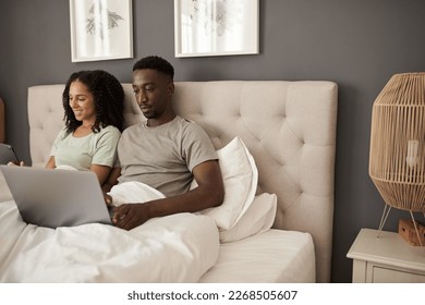Young multiracial couple using different devices in their bed