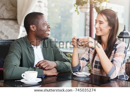 Young multiracial couple using mobile smartphones in cafe. Travel people sharing media in social networks with mobile phones. Technology addiction concept
