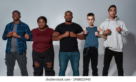 Young Multiracial Crowd Standing Side By Side Holding Hands Under Elbows Against Light Background And Looking At Camera, Widescreen. Stop Racism Concept