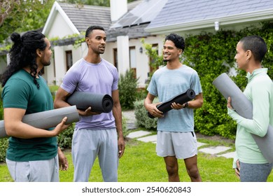 Young multiracial friends holding yoga mats, chatting and smiling outdoors in garden. Fitness, wellness, exercise, yoga class, friendship, outdoor activity - Powered by Shutterstock