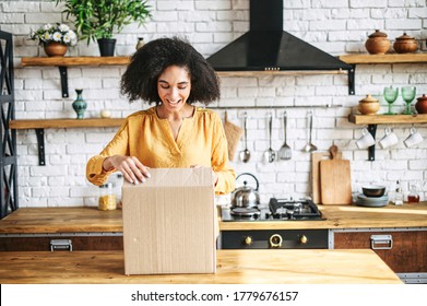 A young multi-racial girl received an online delivery order. Attractive woman with Afro hairstyle unpack the box in the kitchen