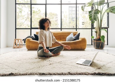 Young Multiracial Latina Woman Meditating At Home With Online Video Meditation Lesson Using Laptop.