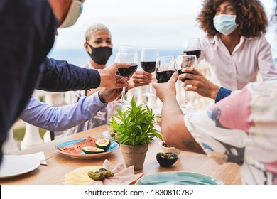 Young Multiracial People Cheering With Red Wine While Wearing Protective Face Mask For Coronavirus - Dinner Together With Safety Measures