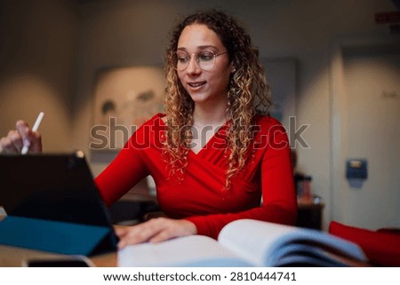 Young multiracial professional using stylus on tablet screen for digital planning, talented woman student multitasking with textbook and gadget in cafe, IT and software development concept.