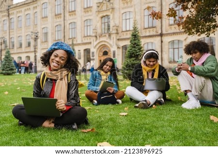 Young multiracial students using gadgets while resting in university garden