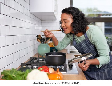 A young multi-racial woman smells and tastes her cooking on the stove - Powered by Shutterstock