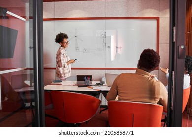 Young multiracial woman standing in front of partners and writing on whiteboard