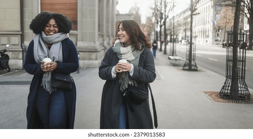 Young multiracial women drinking takeaway coffee walking around the street outdoor during winter time - Cozy beverage and lifestyle concept - Soft focus on asian girl face - Powered by Shutterstock