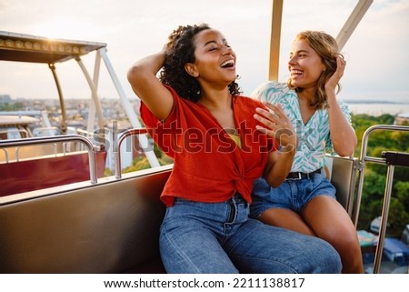 Young multiracial women laughing while riding on ferris wheel in attraction park