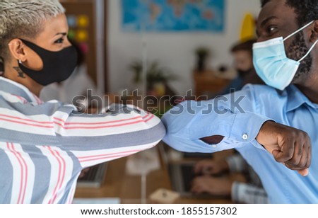 Young multiracial workers wearing face mask doing new social distance greetings bumping elbows inside co-working creative space - Focus on black man arm