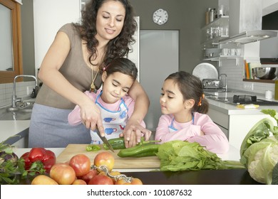 Young Mum Chopping Vegetables With Twin Daughters In A Family Home Kitchen.