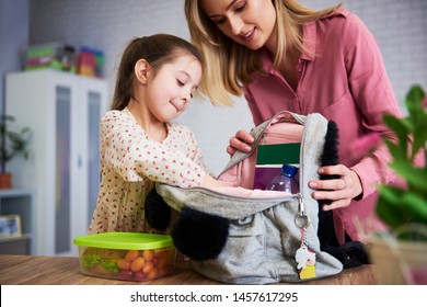 Young mum and daughter packing backpack for the school