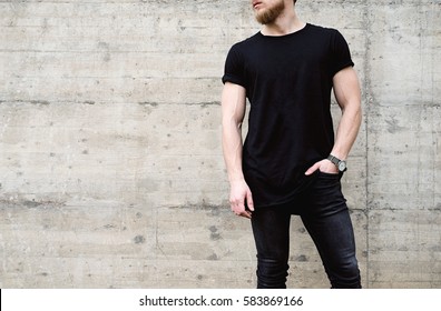 Young Muscular Bearded Man Wearing Black Tshirt And Jeans Posing In Center Of Modern City. Empty Concrete Wall On The Background. Hotizontal Mockup