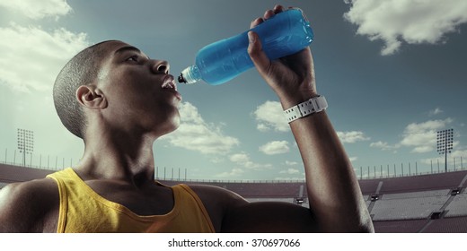 Young Muscular Build Man Drinking Water Of Bottle After Running, Attractive Athlete Resting After Workout Outdoors, Fitness And Healthy Lifestyle Concept. 