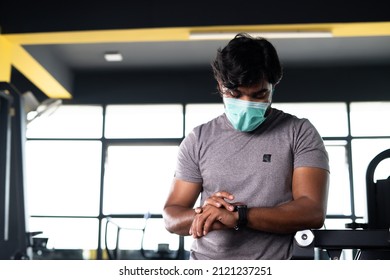 Young Muscular Builder With Medical Face Mask Checking Workout Plan Or Monitoring Hart Rate From Smartwatch At Gym - Concpet Of Healthcare, Technology And Safety Measures During Covid-19 Pandemic.