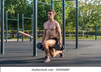 Young Muscular Fitness Male Model Doing Dumbbell Lunge Exercises In The Park.