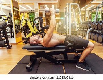 Young muscular fitness man trains pectoral muscles while lying on a bench with dumbbells in his arms at the gym